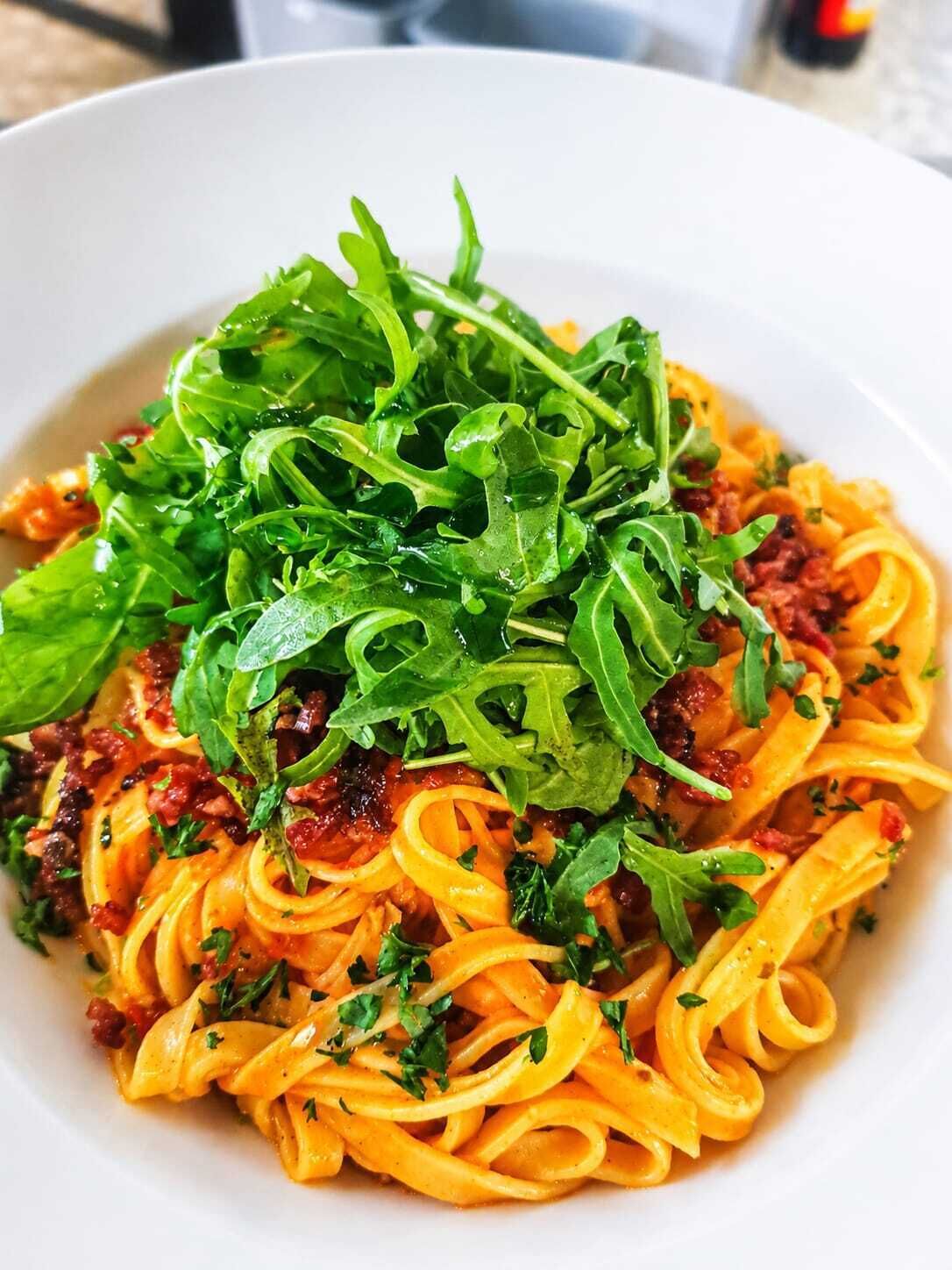 Un plato de pasta con salsa de tomate, aderezado con rúcula y hierbas.