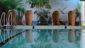A swimming pool with clear water, surrounded by lounge chairs and a mural of a tropical scene.