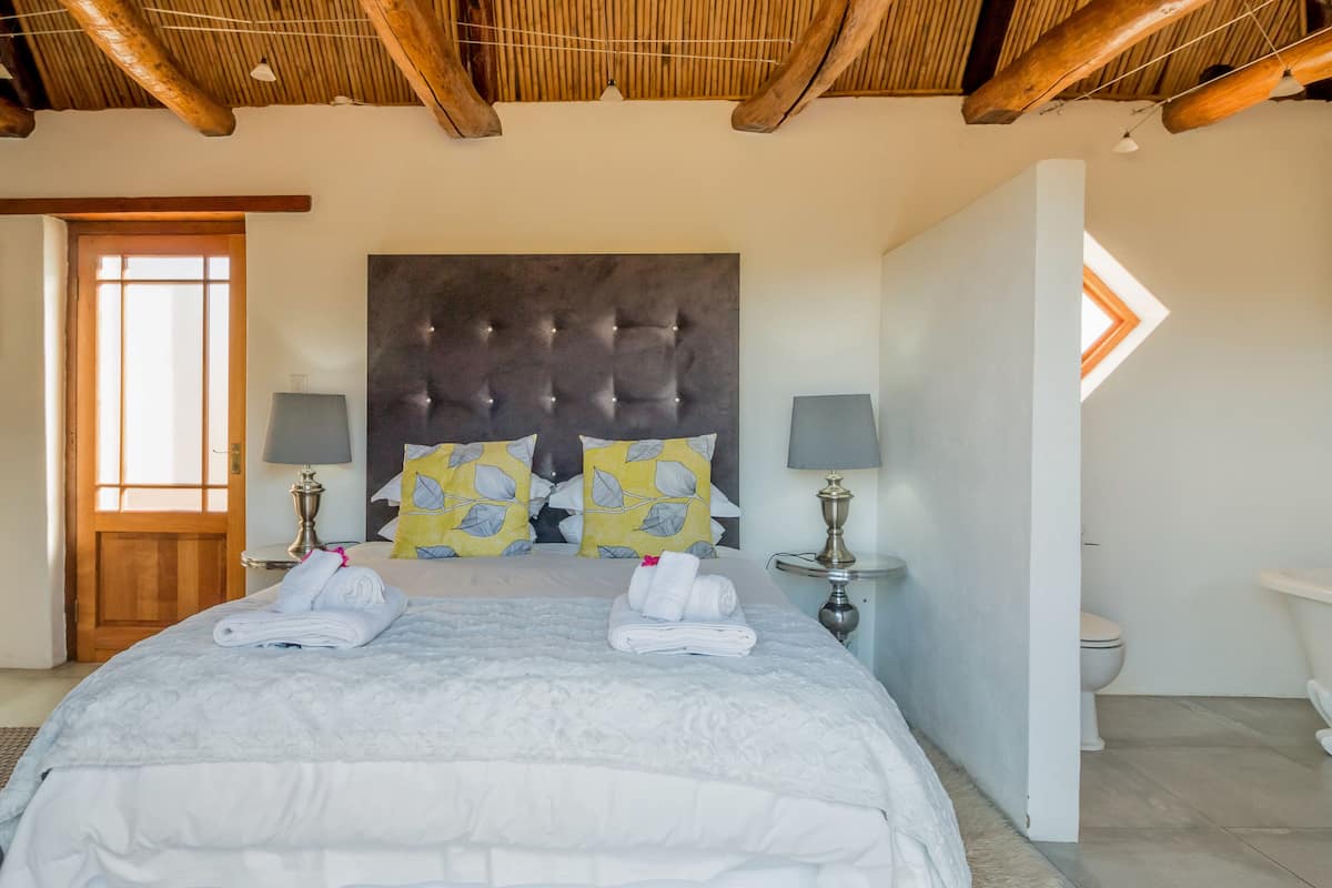 Une chambre à coucher avec un grand lit, deux lampes de chevet, une tête de lit avec des lumières intégrées, un tableau au mur et un plafond en bois.