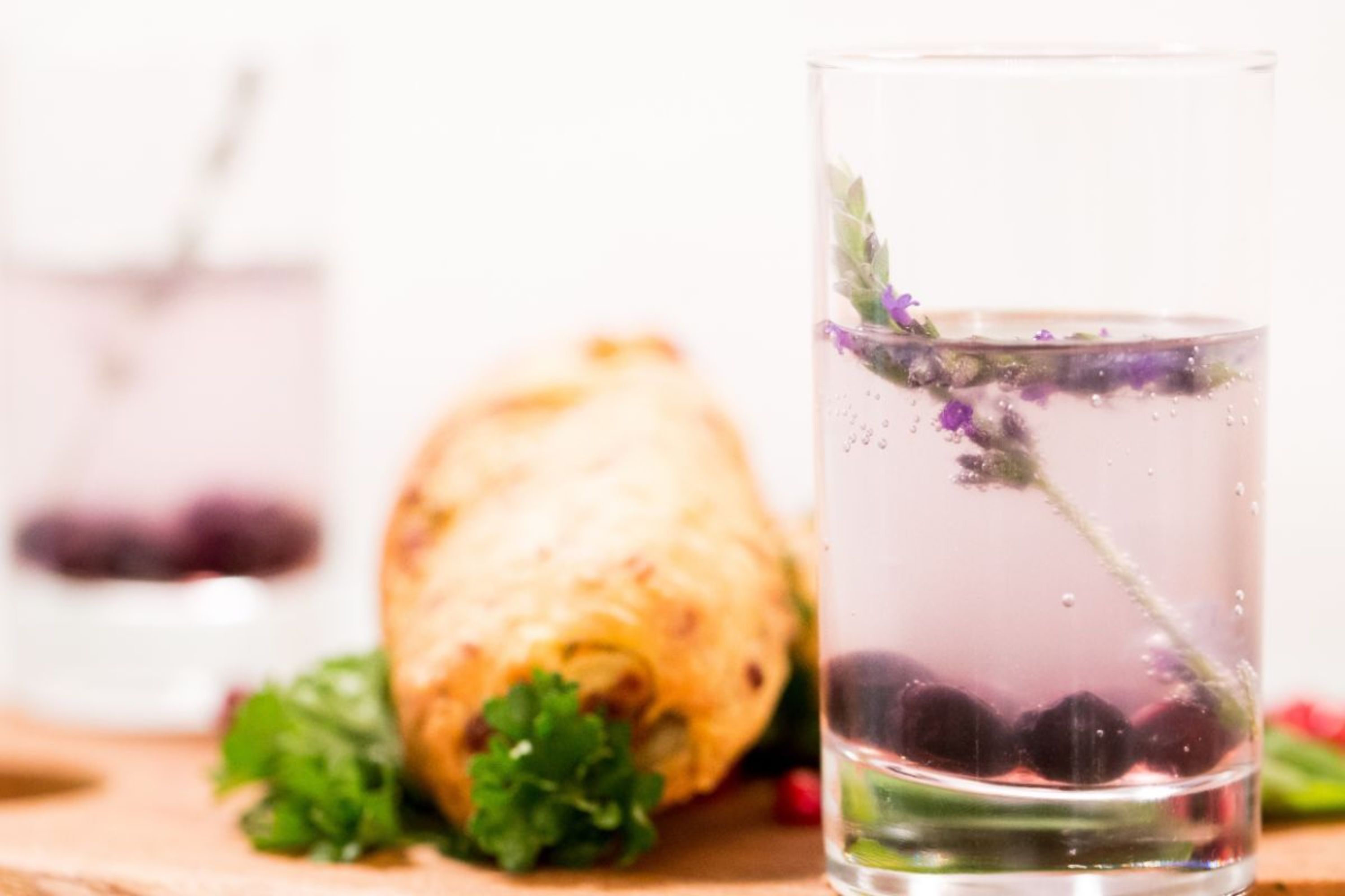 Un verre d’eau avec une tige de fleur, une pâtisserie et quelques feuilles vertes sur une surface en bois.