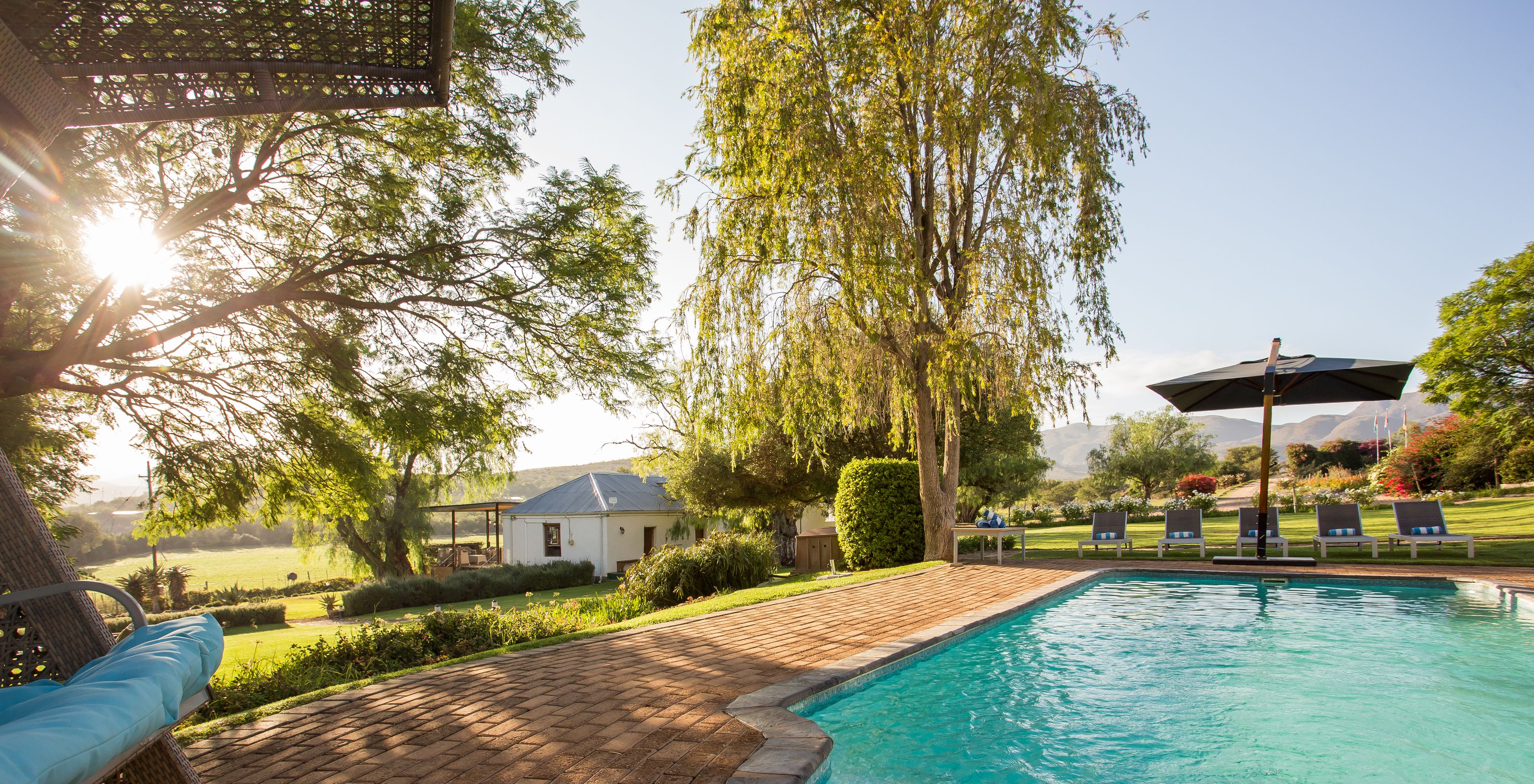 Zwembad met ligbedden, een pergola en uitzicht op een huis en landschap.