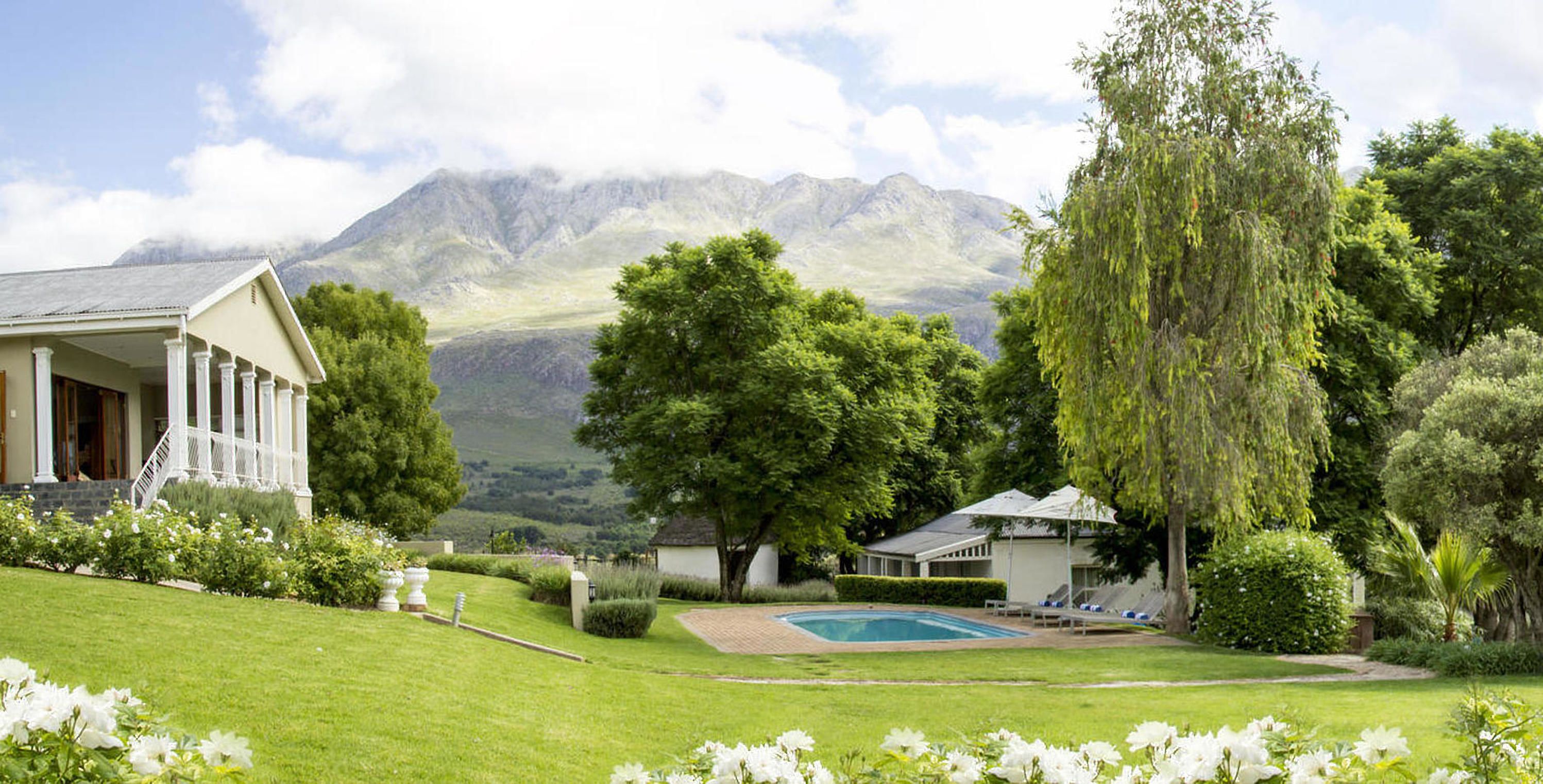 A house with a pool, surrounded by lush greenery and mountains in the background.