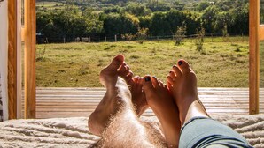 A person relaxing with feet up on a wooden deck, overlooking a green landscape with mountains in the distance. - Swartberg Country Manor (Oudtshoorn)