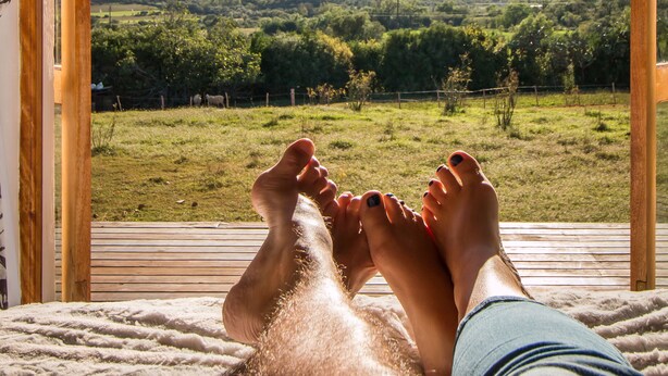 A person relaxing with feet up on a wooden deck, overlooking a green landscape with mountains in the distance.