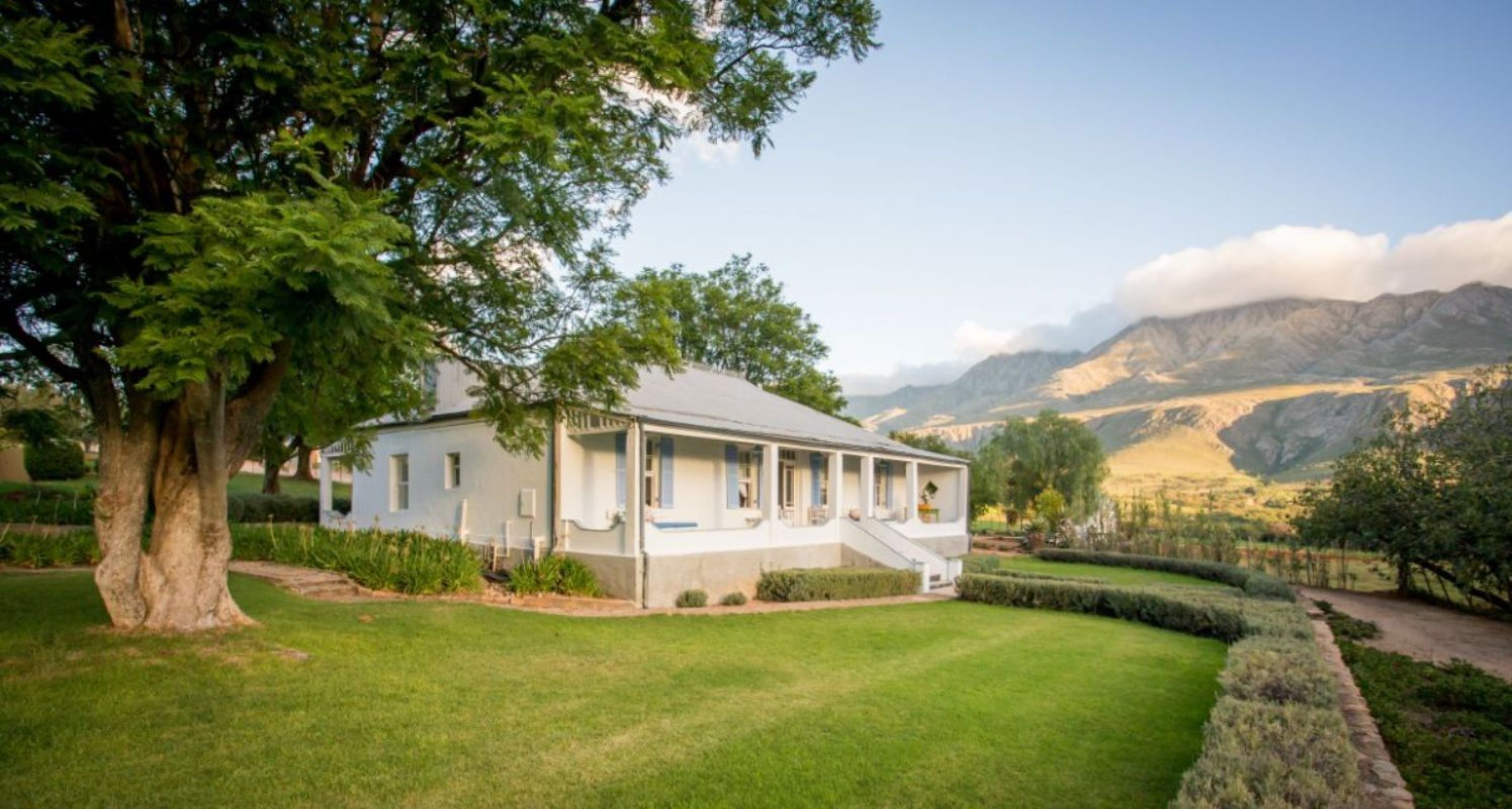 A two-story house with a covered porch and a well-maintained lawn, surrounded by mountains and trees.