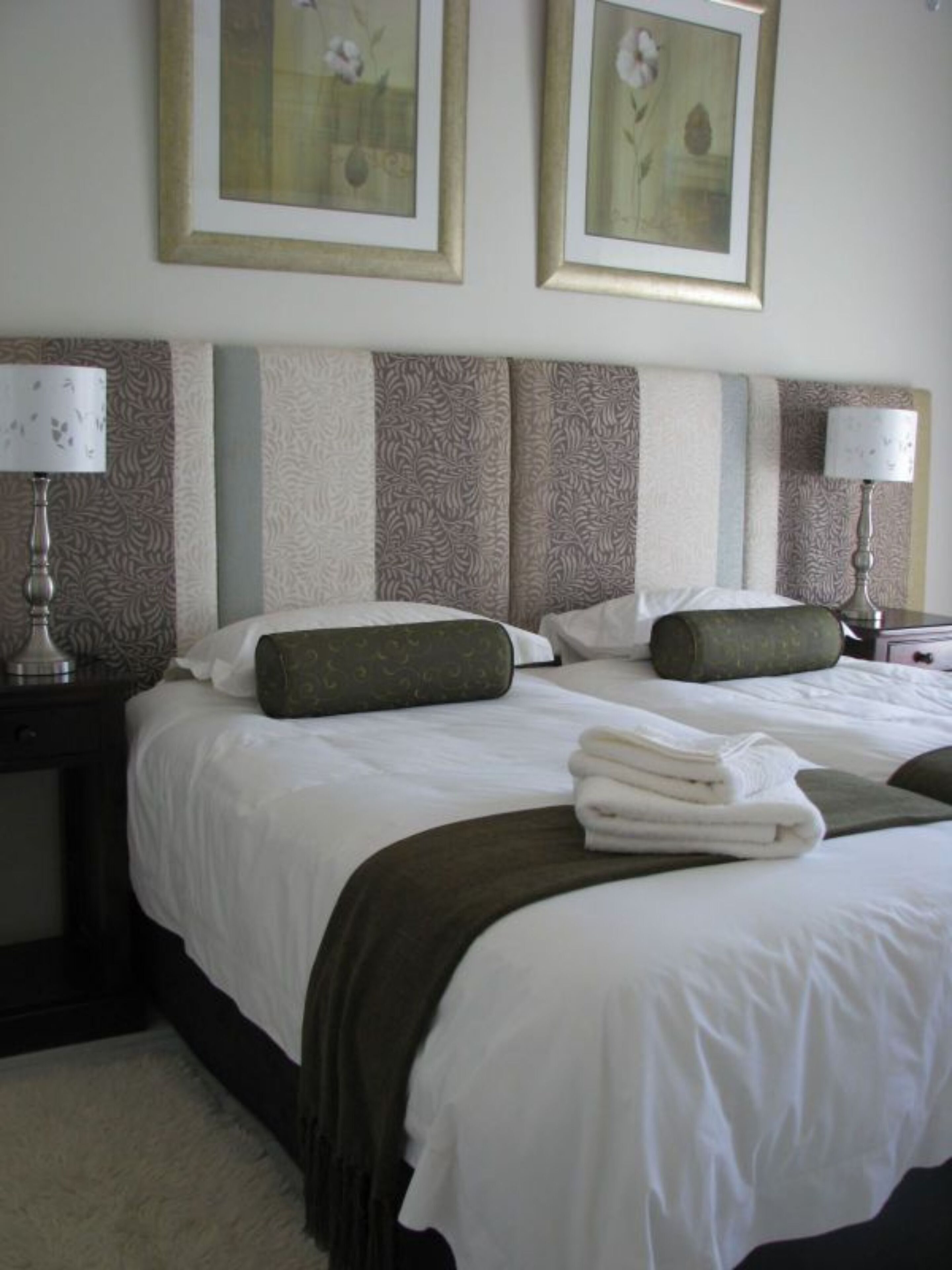 Habitación de hotel con una cama grande, dos almohadas, una mesita de noche con una lámpara y dos cuadros enmarcados en la pared.