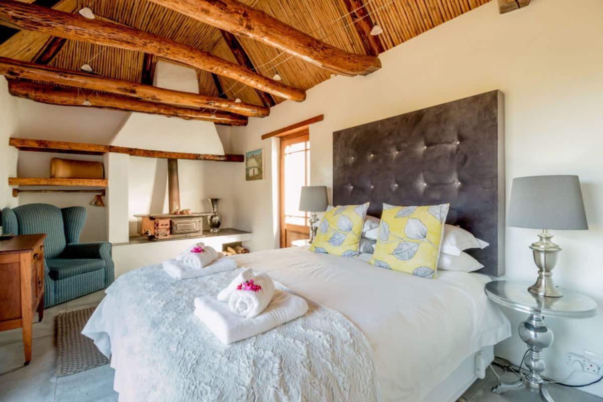 Une chambre avec un grand lit, des poutres en bois, une table de chevet, une lampe et une chaise.