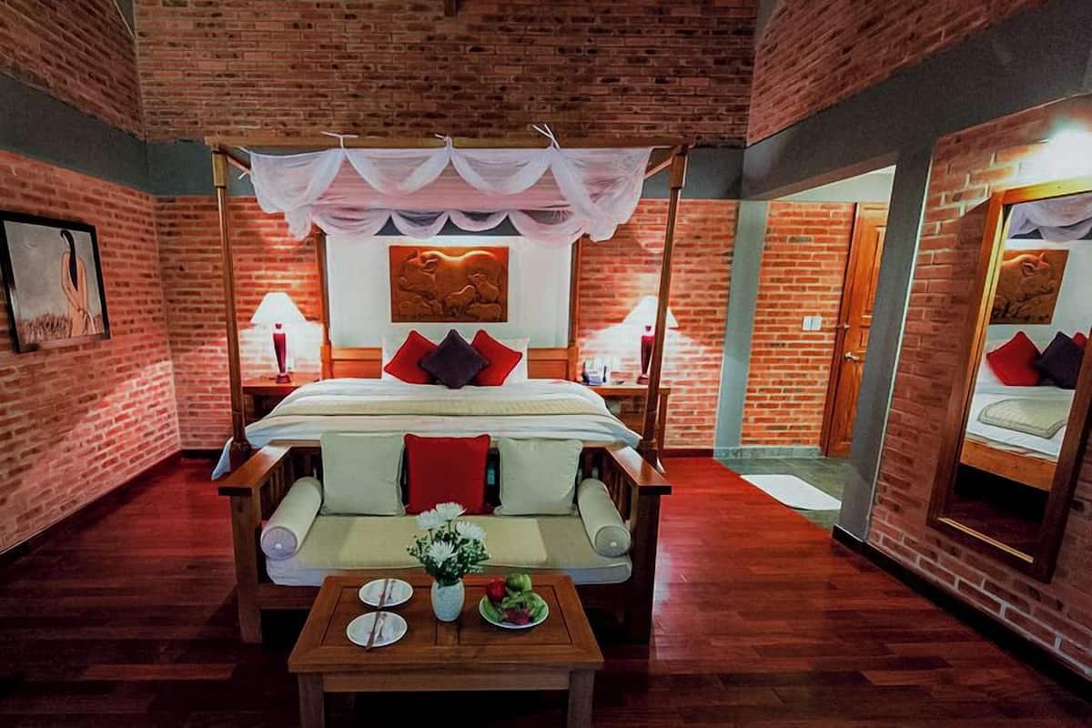 A room with a bed, a sofa, a table with plates and a vase, and a mirror on the wall.