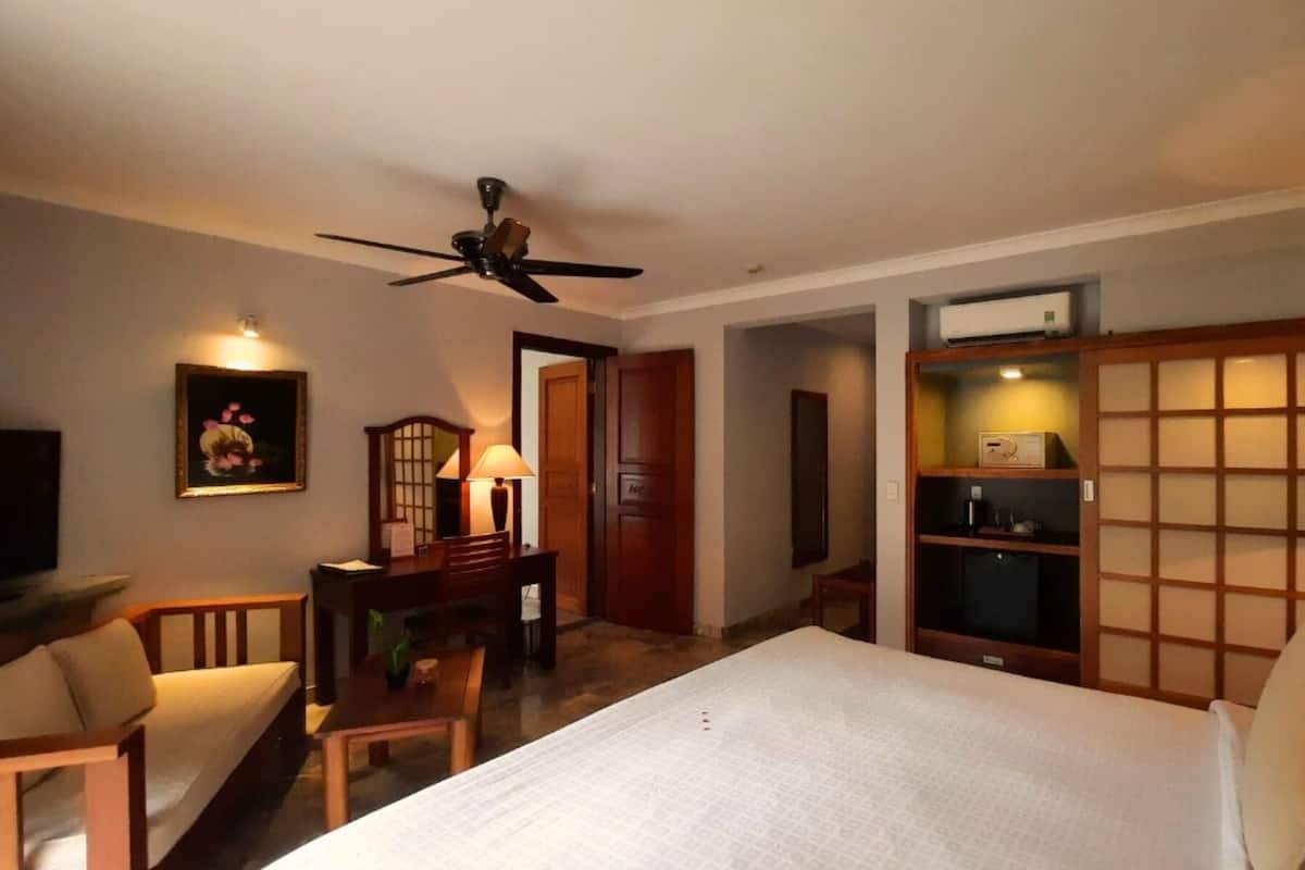 A hotel room with a bed, a desk, a chair, a television, and a ceiling fan.