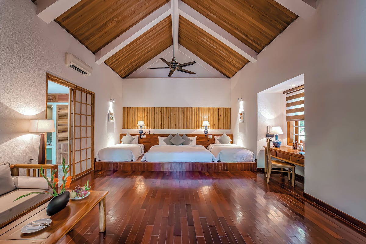 A hotel room with a wooden ceiling, a bed with two pillows, a bedside table, a chair, and a wooden floor.