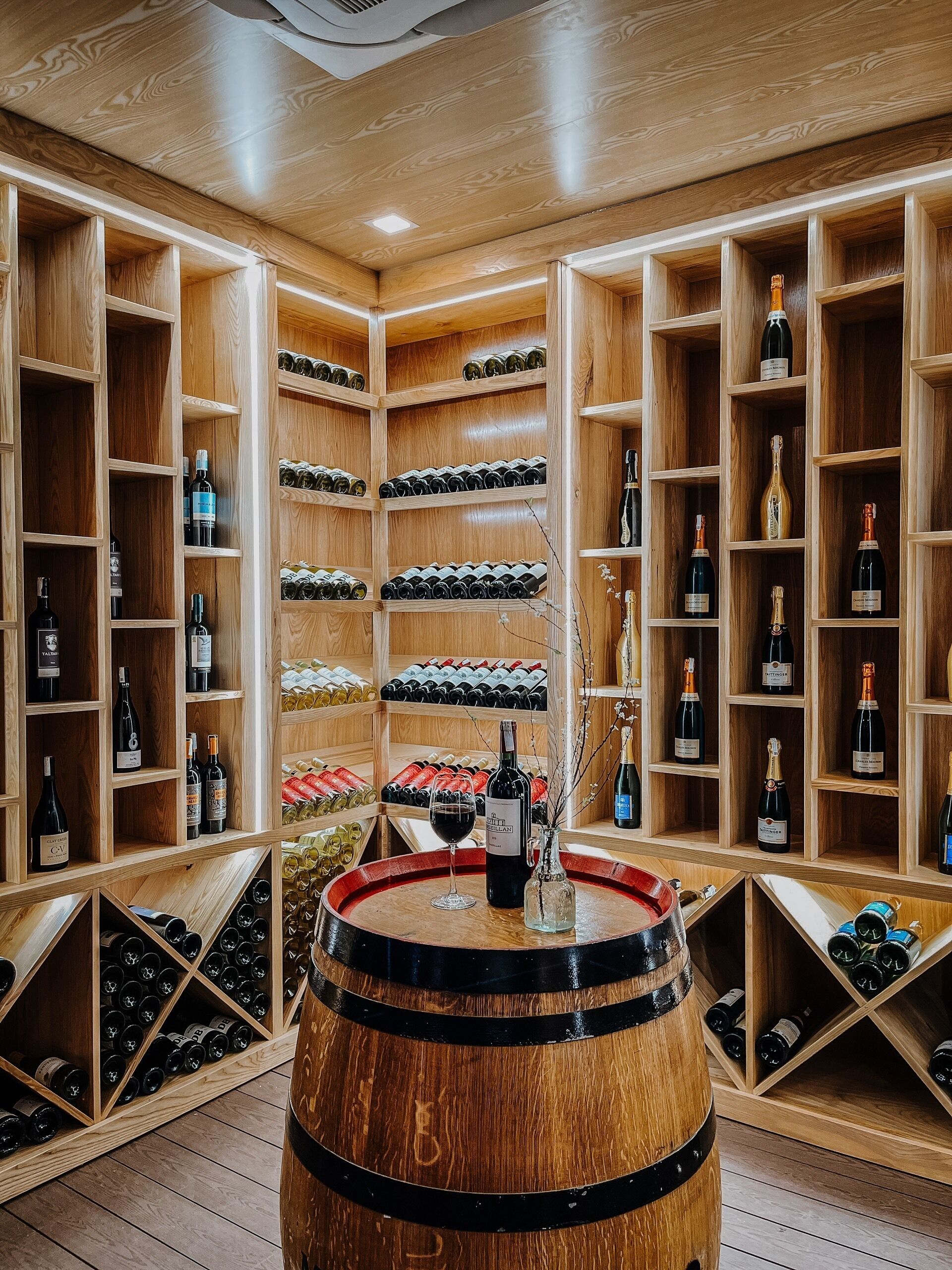 Una cantina vinicola con scaffali in legno e botti, contenente diverse bottiglie di vino.