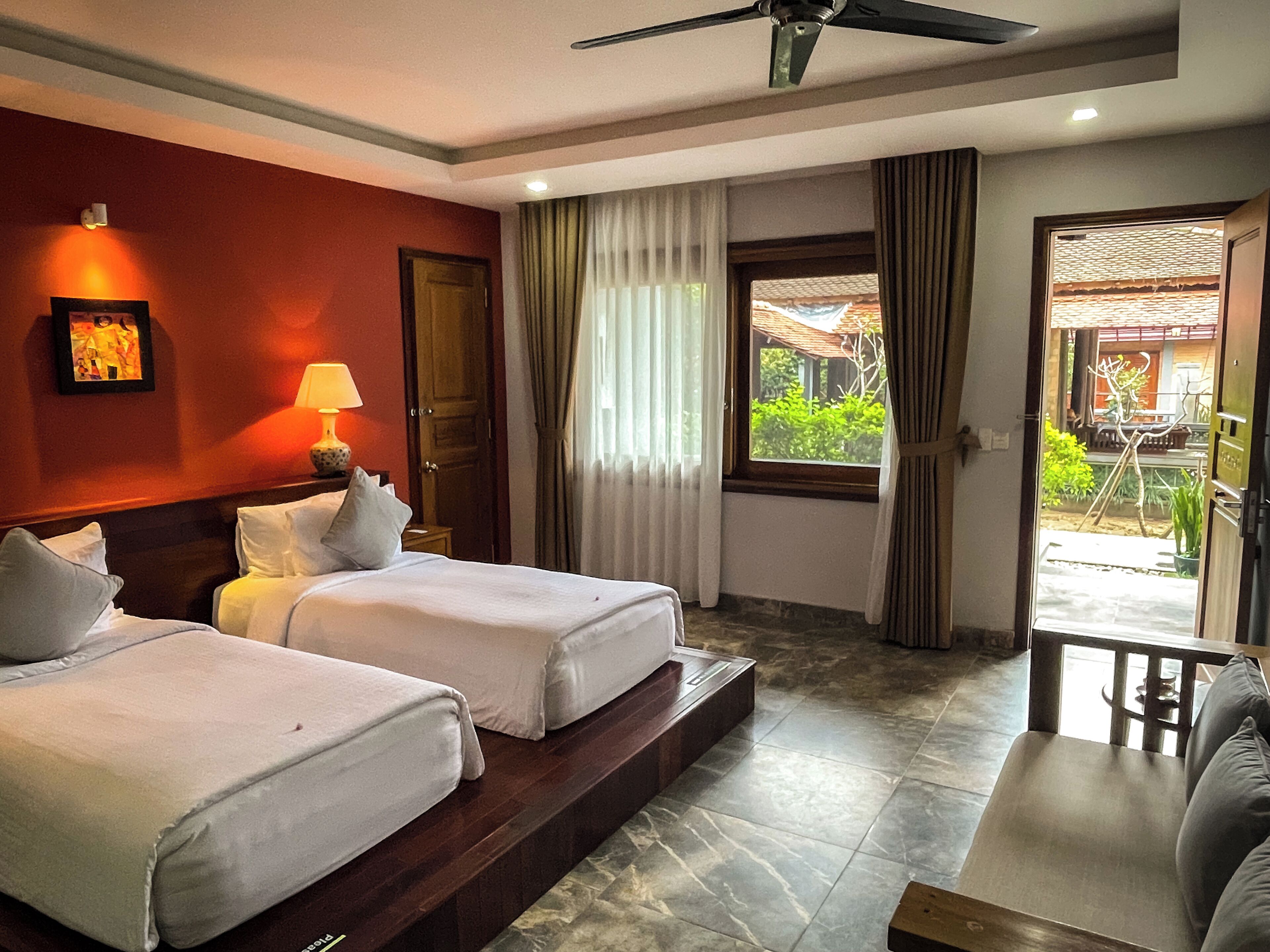 A hotel room with two beds, a sitting area, a ceiling fan, and a view of the outdoors.