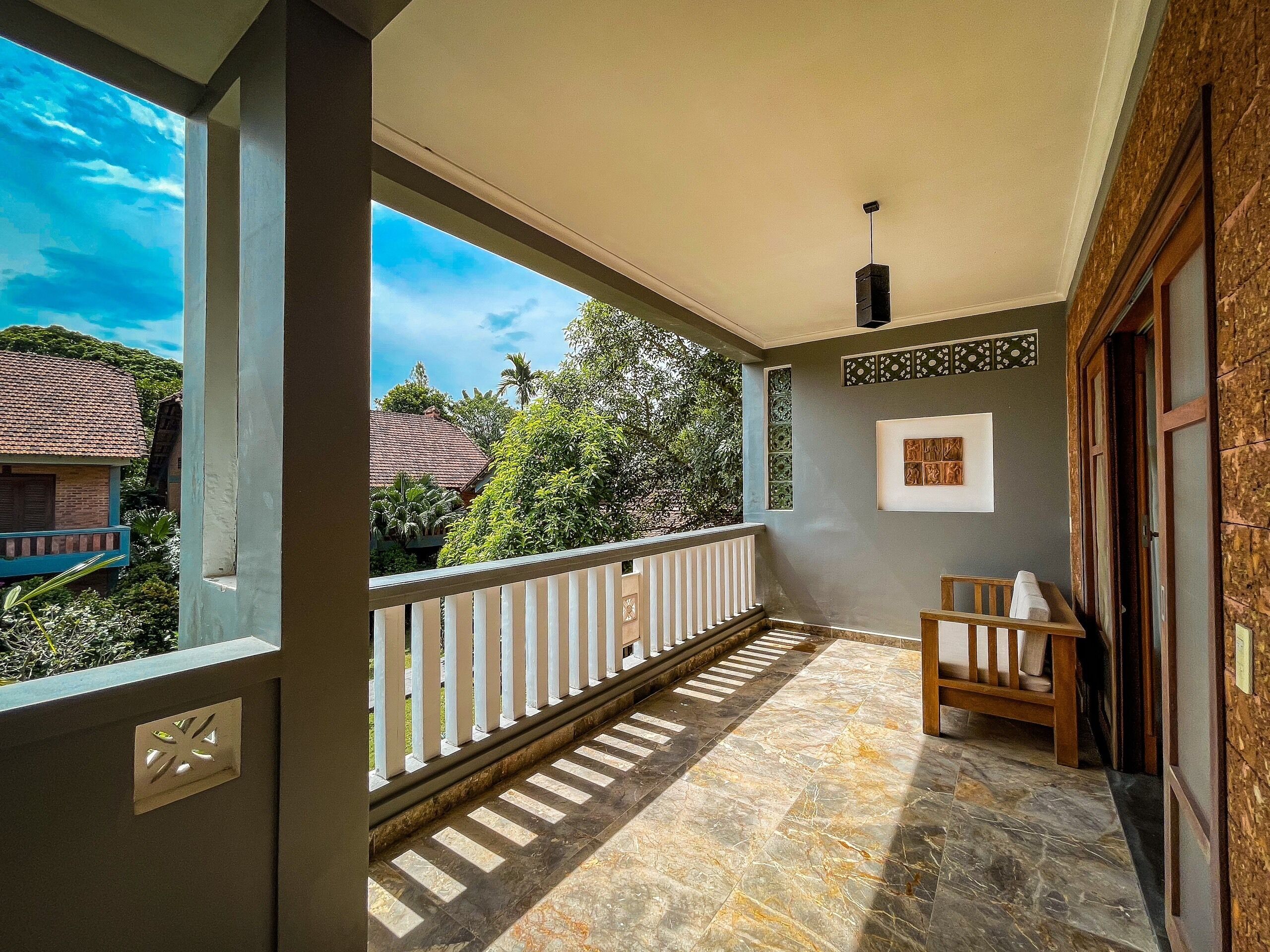 A balcony with a view of houses and trees, a tiled floor, and a wooden bench.