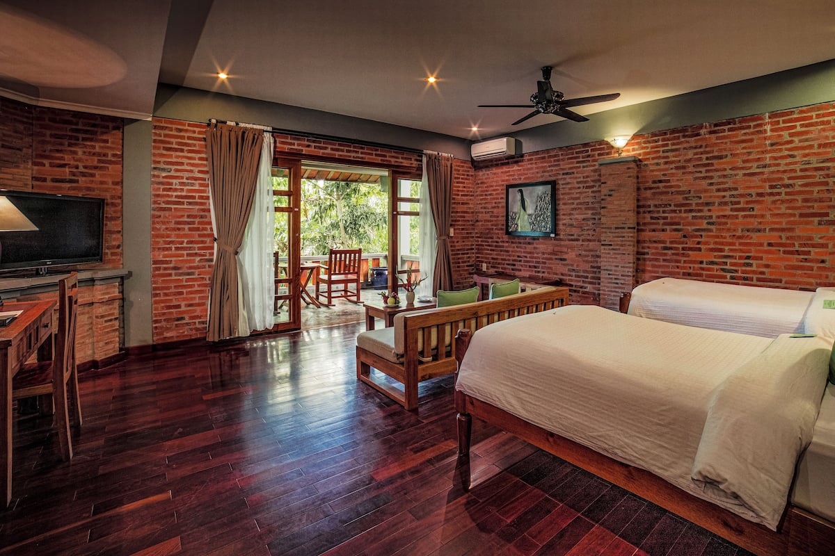 A hotel room with a brick wall, wooden furniture, a TV, and a bed.