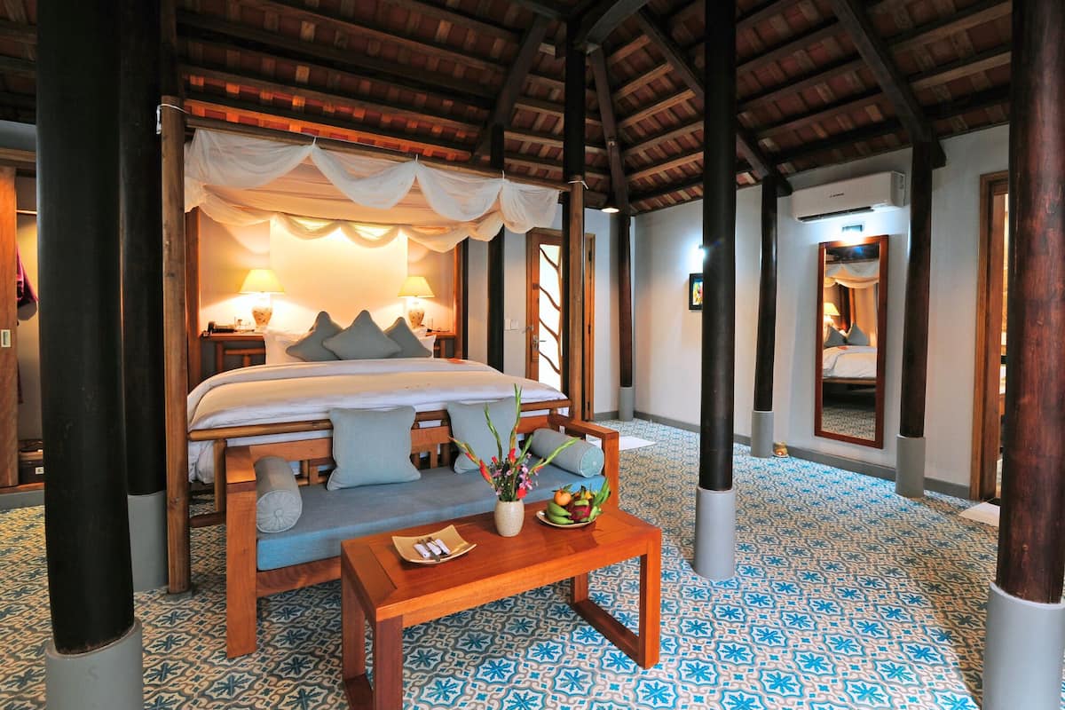 A hotel room with a large bed, two bedside lamps, a wooden table with a vase of flowers, and a patterned floor.