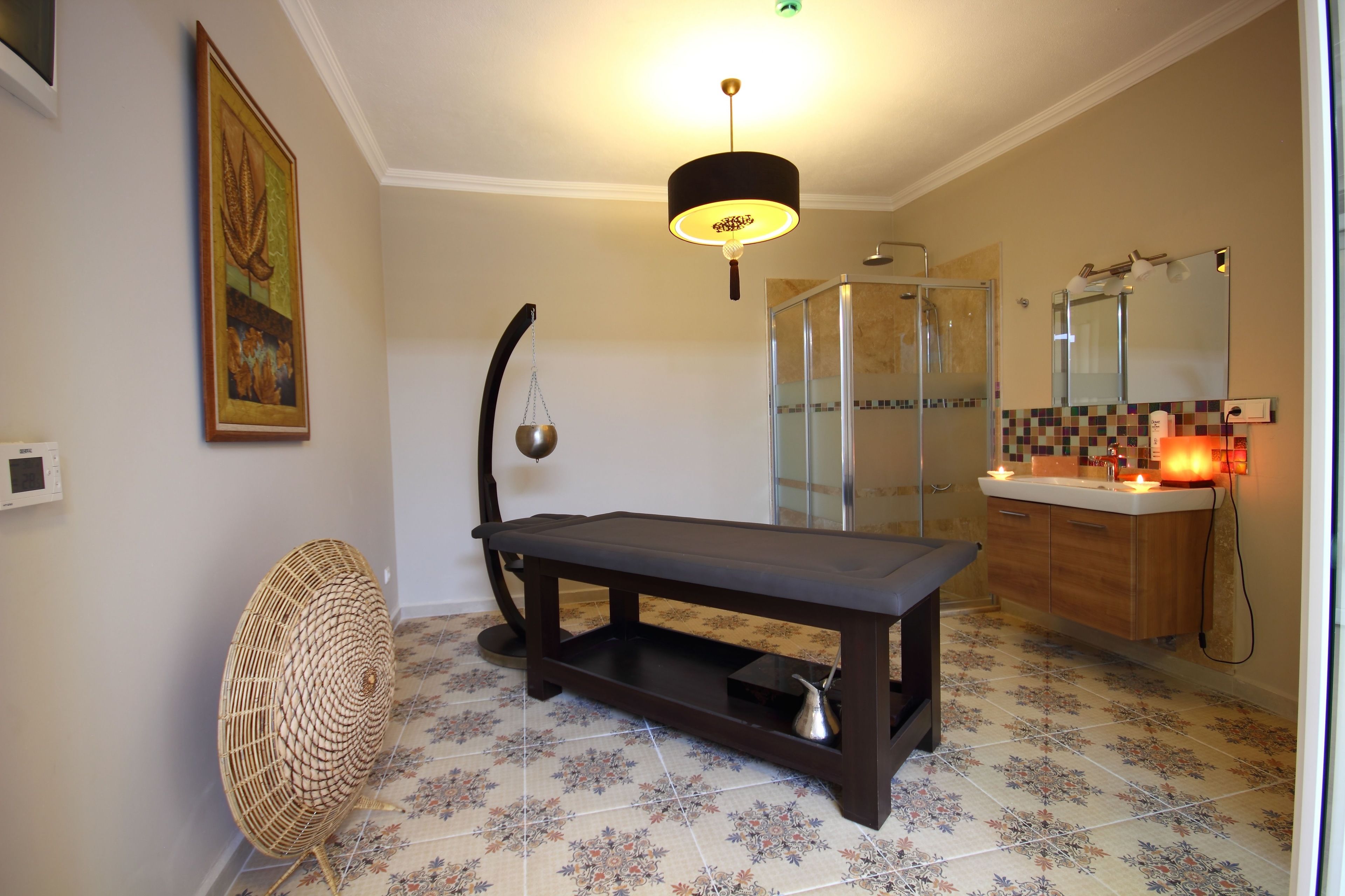 A bathroom with a shower, a sink with a mirror, a table, and a fan.