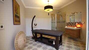 A bathroom with a shower, a sink with a mirror, a table, and a fan.