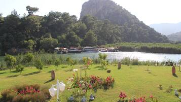 Un jardin au bord du lac, avec des bateaux, une grande formation rocheuse et une végétation luxuriante.