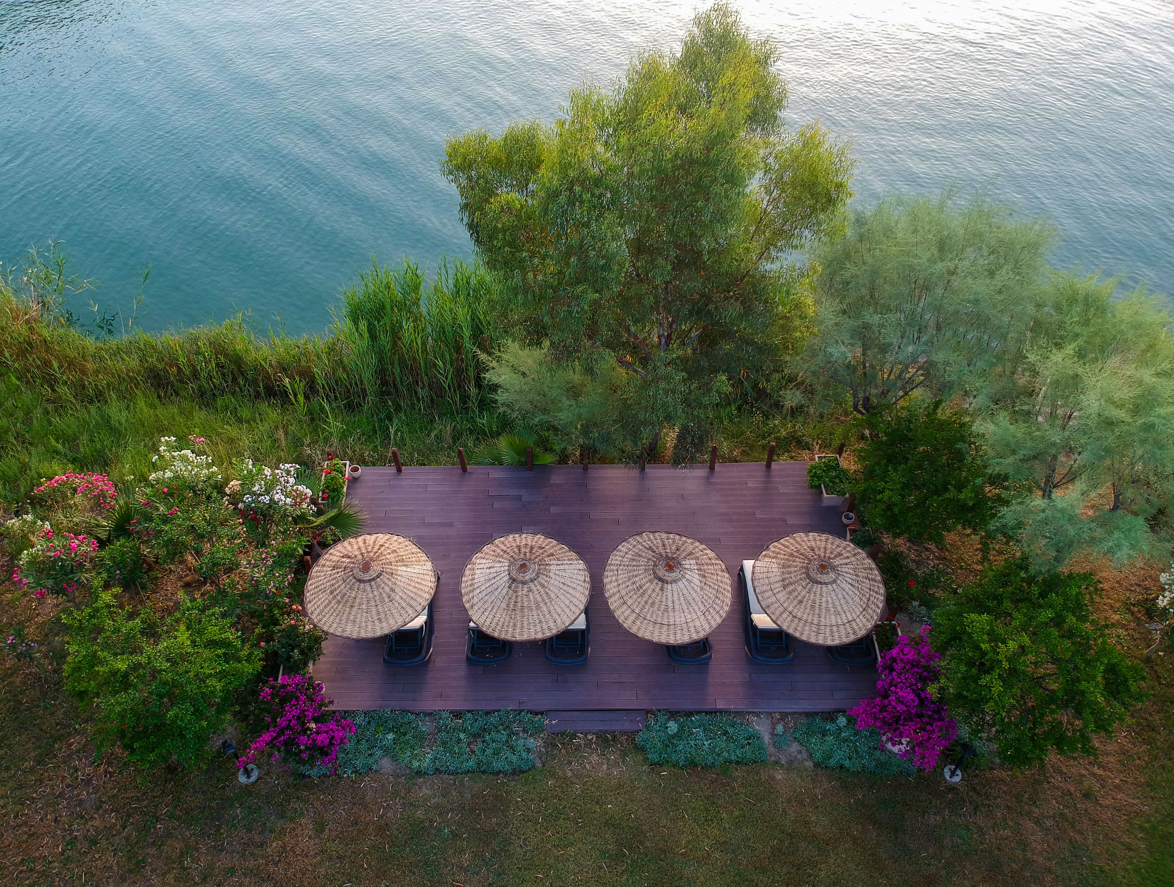 An aerial view of a deck with four tables and umbrellas, surrounded by lush greenery and a body of water.