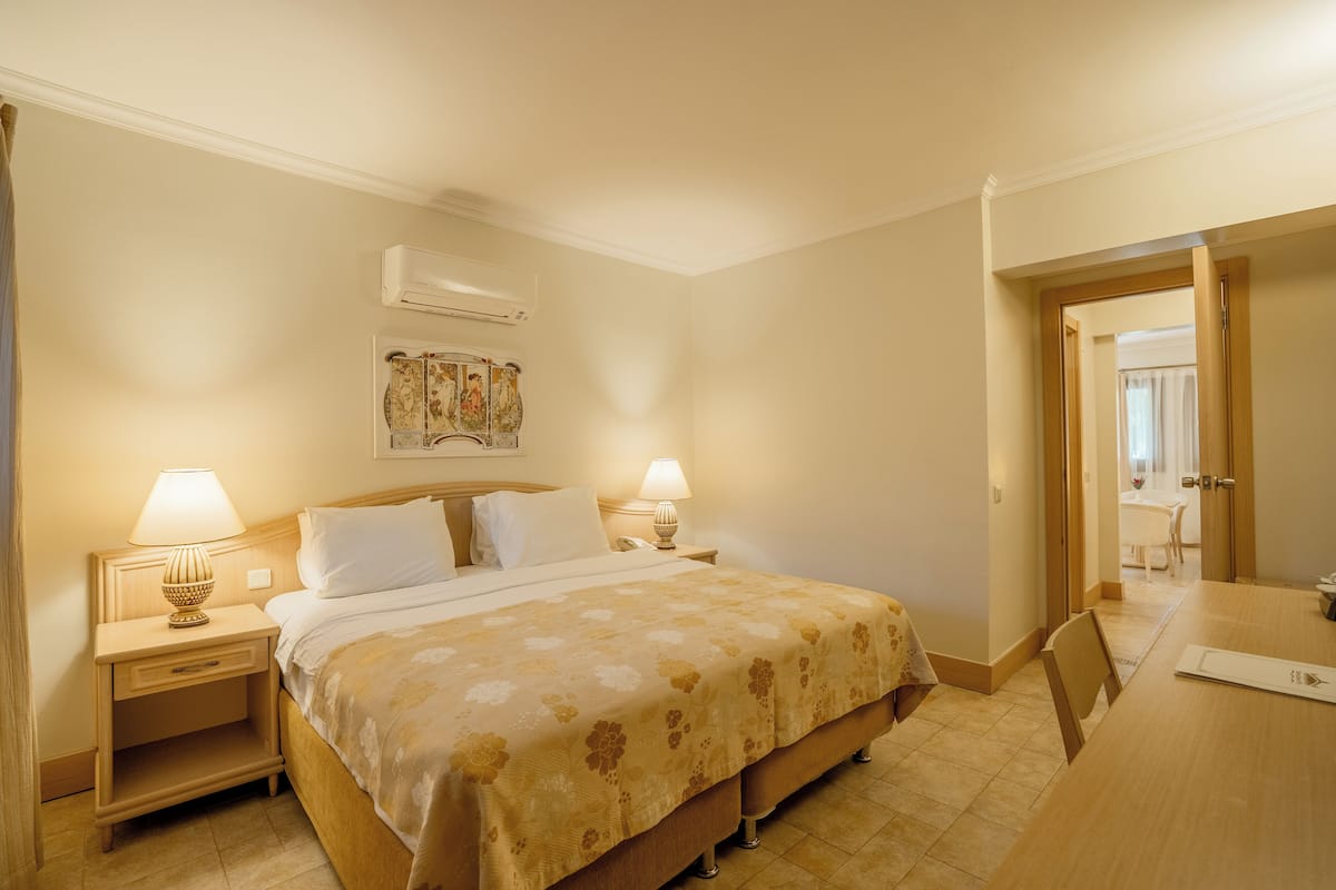 A hotel room with a large bed, two bedside lamps, a wooden nightstand, a small table, and a chair.