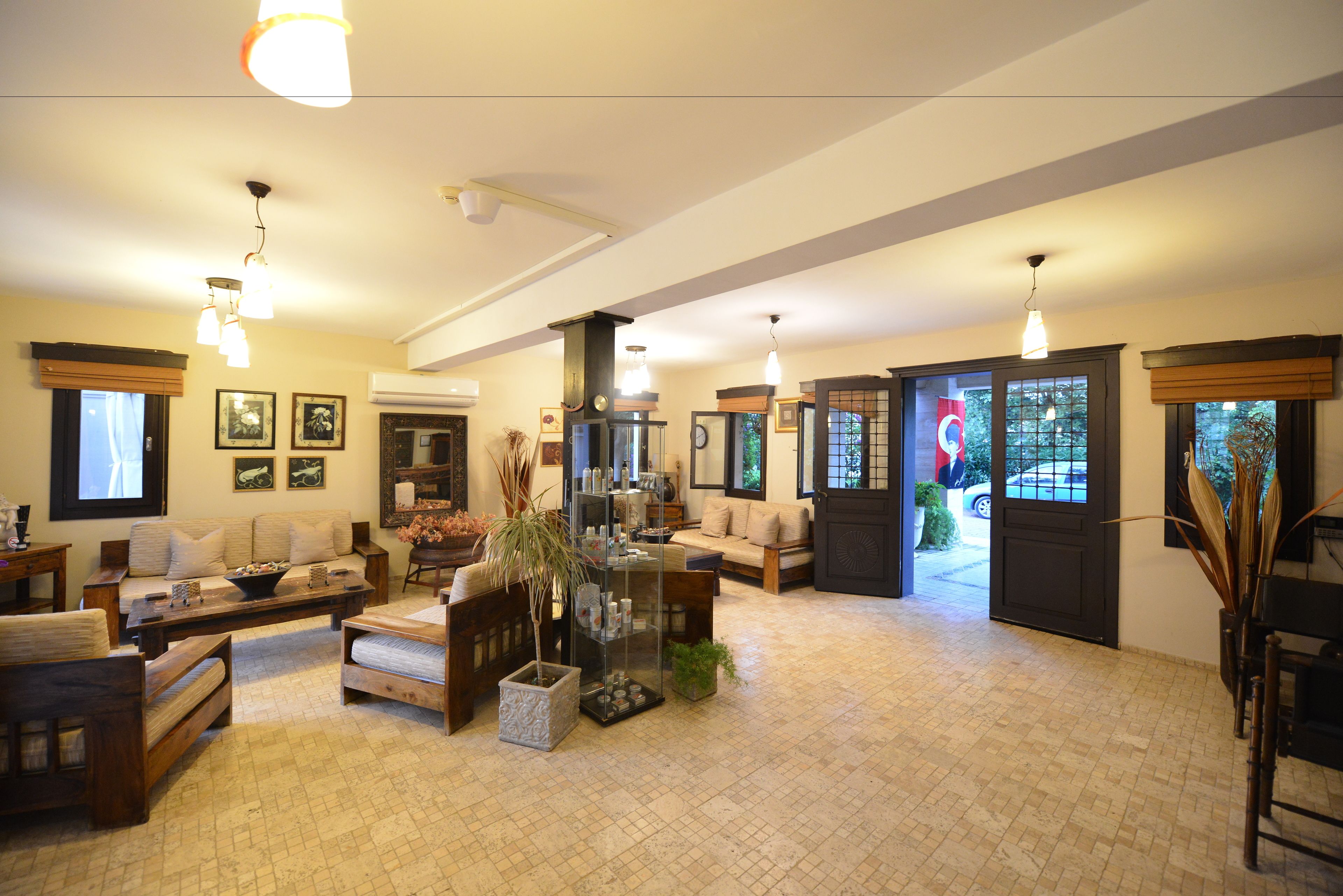 A spacious living room with a large sofa, a coffee table, and a fireplace. There are several framed pictures on the walls and a potted plant in the center.