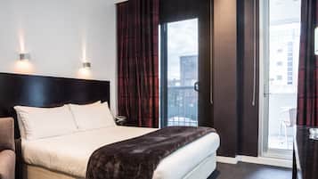 A hotel room with a bed, a chair, a nightstand, and a view of the outside through a glass door.