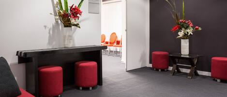 A modern reception area with a black reception desk, red seating, and two vases with flowers.