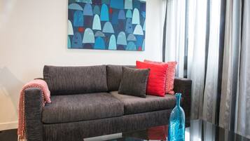 A modern living room with a grey sofa, red and white cushions, a blue vase, and a large abstract painting on the wall.
