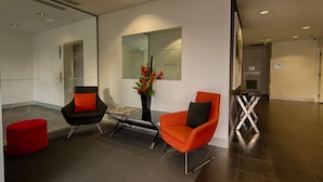 A modern waiting area with two chairs, a red ottoman, and a glass table. - Adara Hotel Richmond (Richmond)