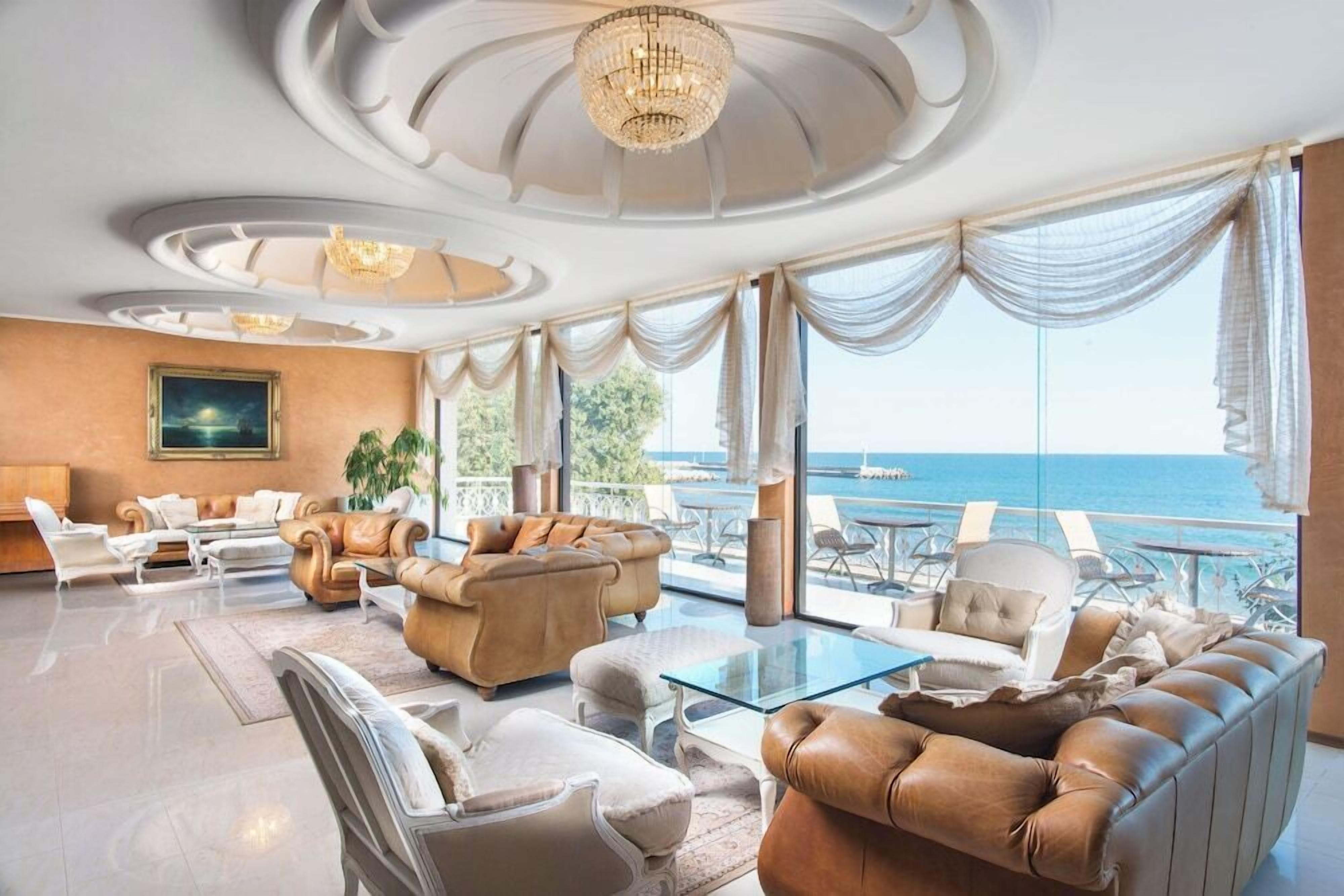 Uma sala de estar luxuosa com uma grande janela com vista para o mar, móveis elegantes e um candelabro.