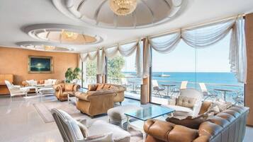 Uma sala de estar luxuosa com uma grande janela com vista para o mar, móveis elegantes e um candelabro.