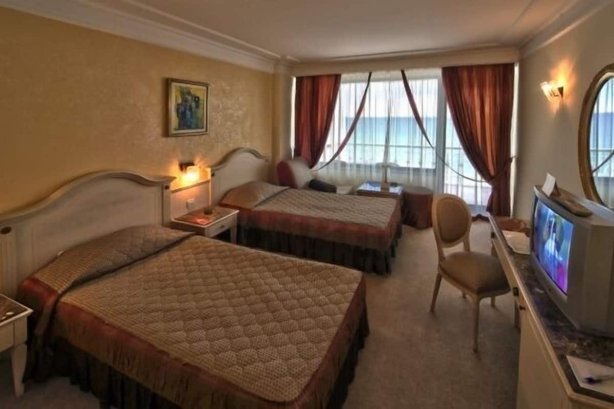 Habitación de hotel con dos camas, un escritorio con computadora, una silla y un televisor.