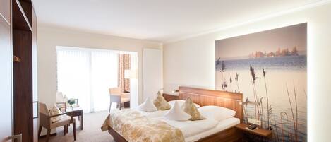 Habitación de hotel con una cama grande, un escritorio y una silla. En la pared, se observa un cuadro de un lago.
