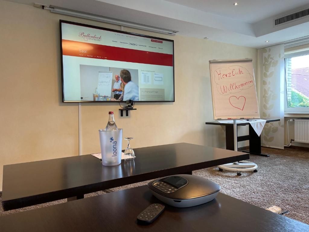 A conference room with a large screen displaying a website, a whiteboard with a message, a bottle of water, and a remote control on a table.