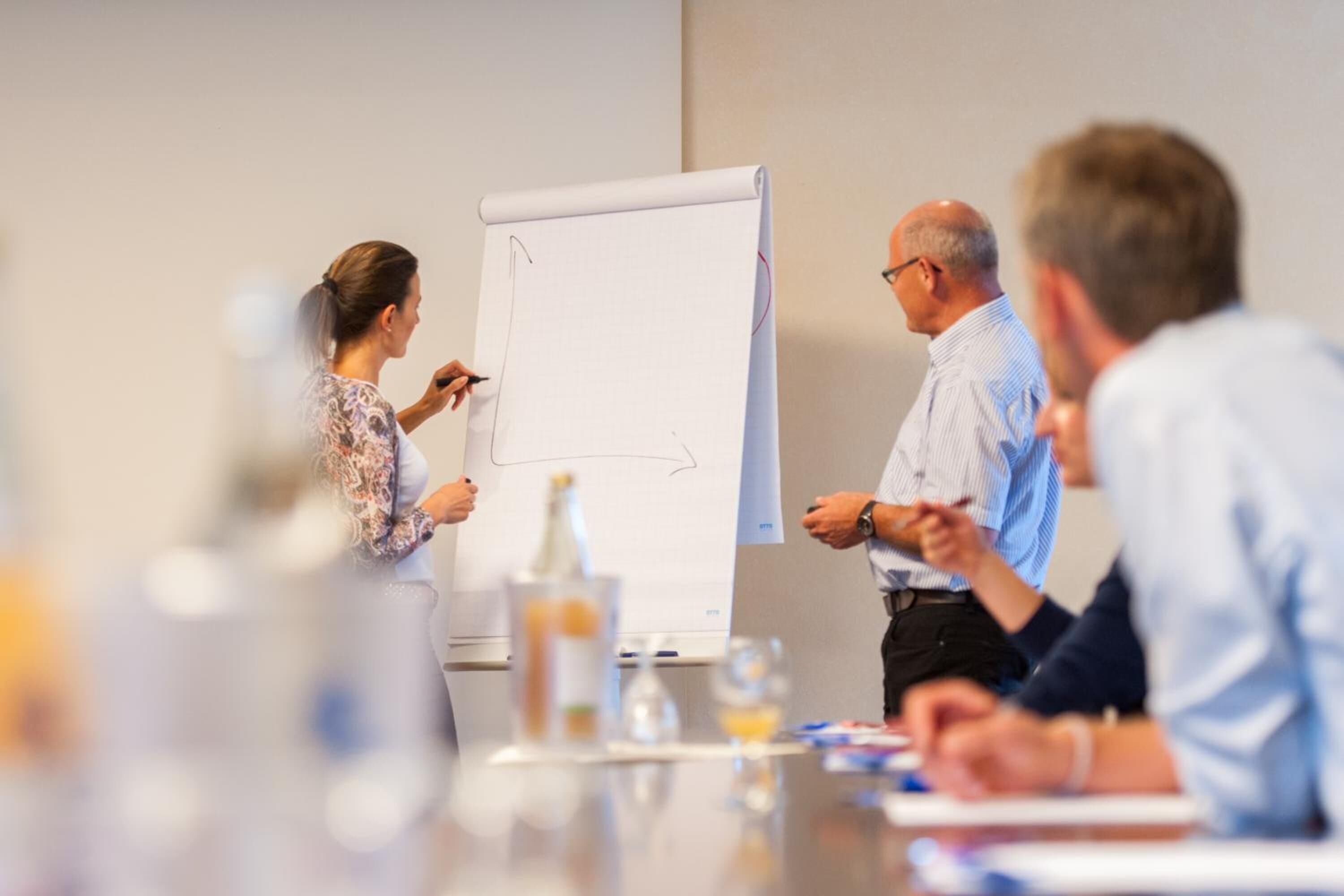 A meeting with a whiteboard, a bottle, and documents on a table.
