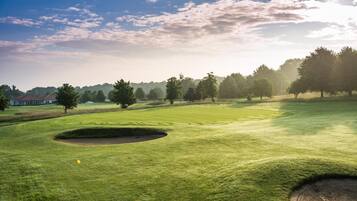 Ein Golfplatz mit Bunker, Bäumen und blauem Himmel.