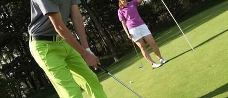 A golf course with a putting green and trees in the background.
