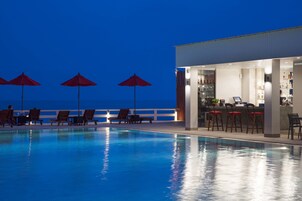 Zona de piscina con sillones de descanso y sombrillas, un bar y vistas al mar.