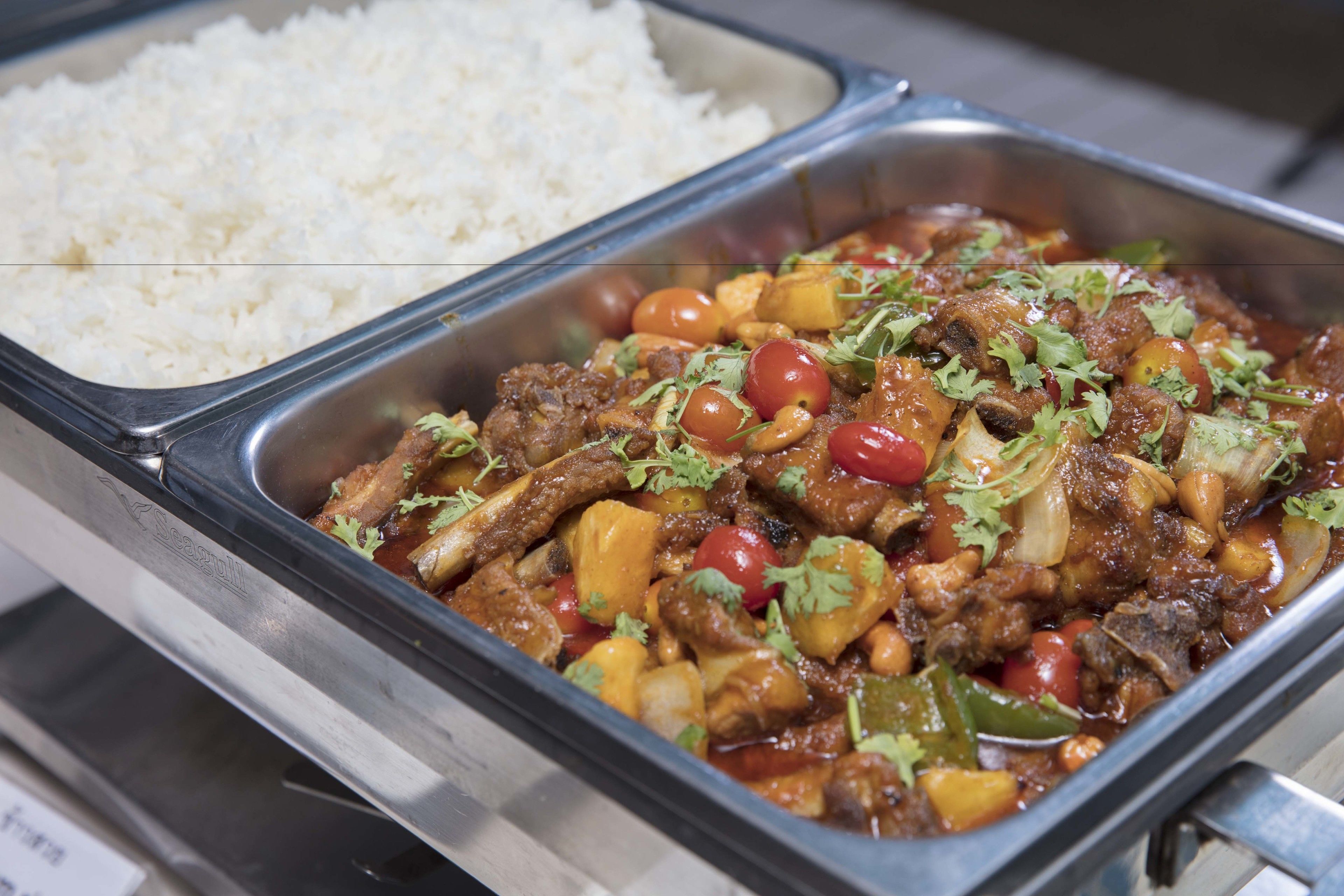 A buffet with white rice and a meat dish garnished with herbs.