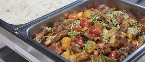 A buffet with white rice and a meat dish garnished with herbs.