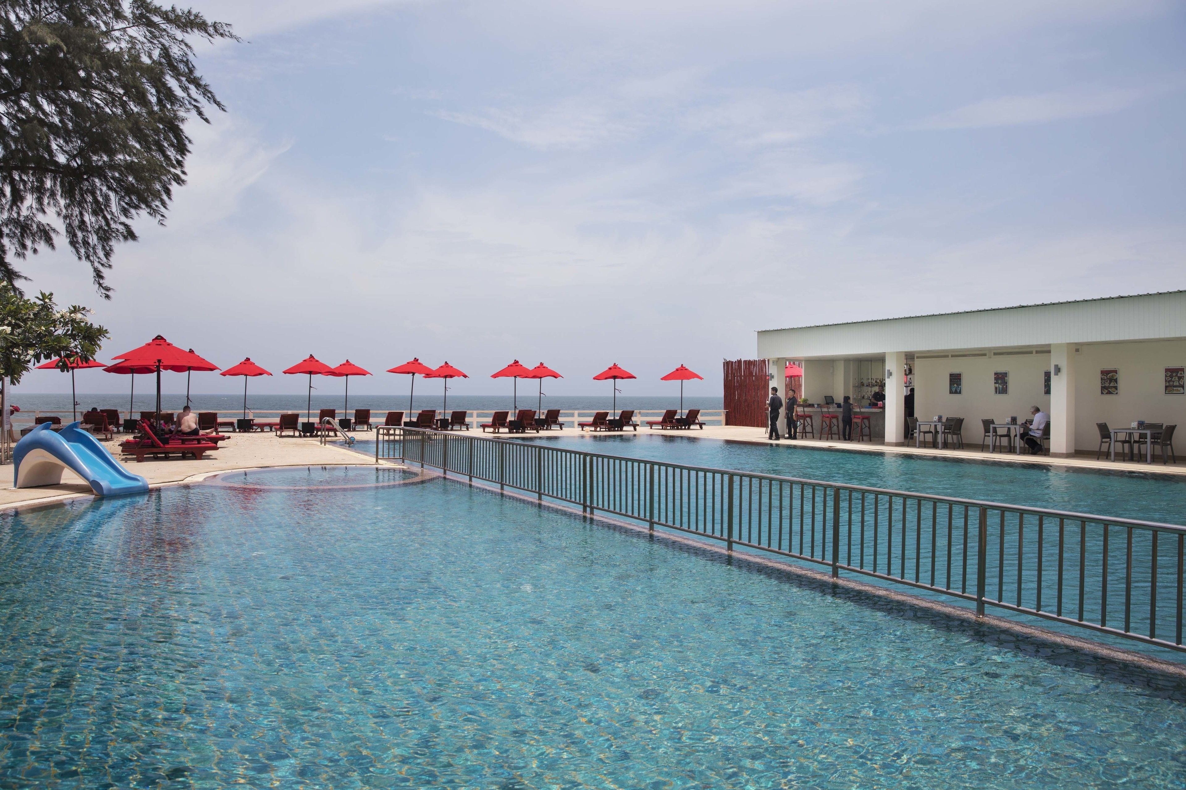 Una piscina con tobogán, sombrillas rojas y sillas de descanso.