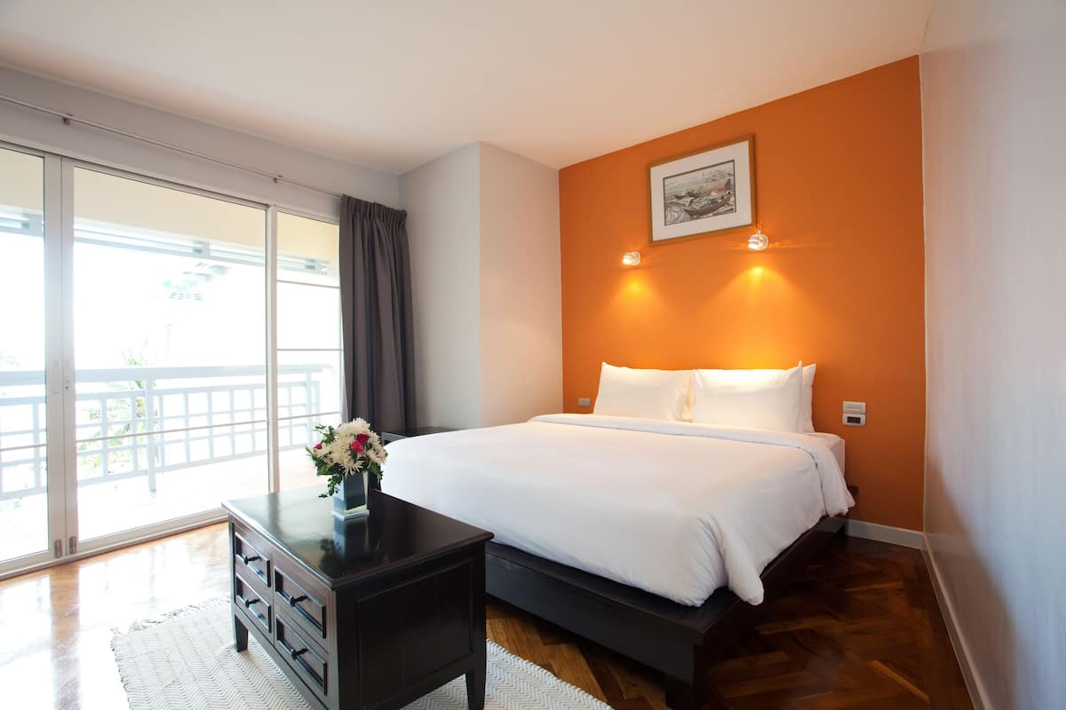 A bedroom with a bed, a dresser, a nightstand, and a large window with a view of a balcony.