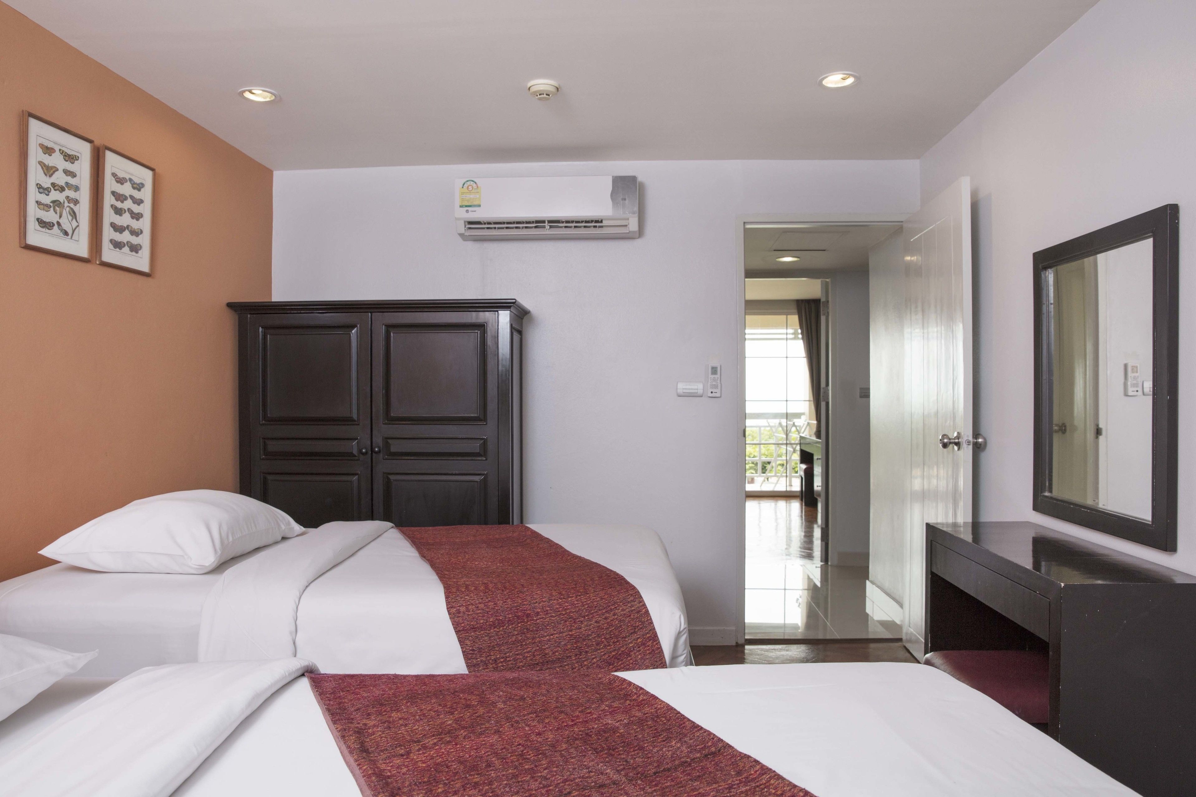 A hotel room with a bed, a wardrobe, a mirror, and an air conditioning unit on the wall.
