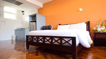 Une chambre à coucher avec un cadre de lit en bois, du linge de lit blanc, une armoire grise et un mur d’accent orange.