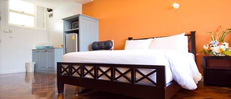 Een slaapkamer met een houten bedframe, witte beddengoed, een grijze garderobe en een oranje accentmuur.