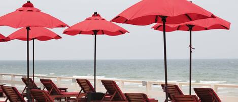 Un área de descanso frente a la playa con sillones de madera y sombrillas rojas.