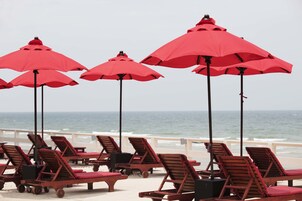 Un área de descanso frente a la playa con sillones de madera y sombrillas rojas.