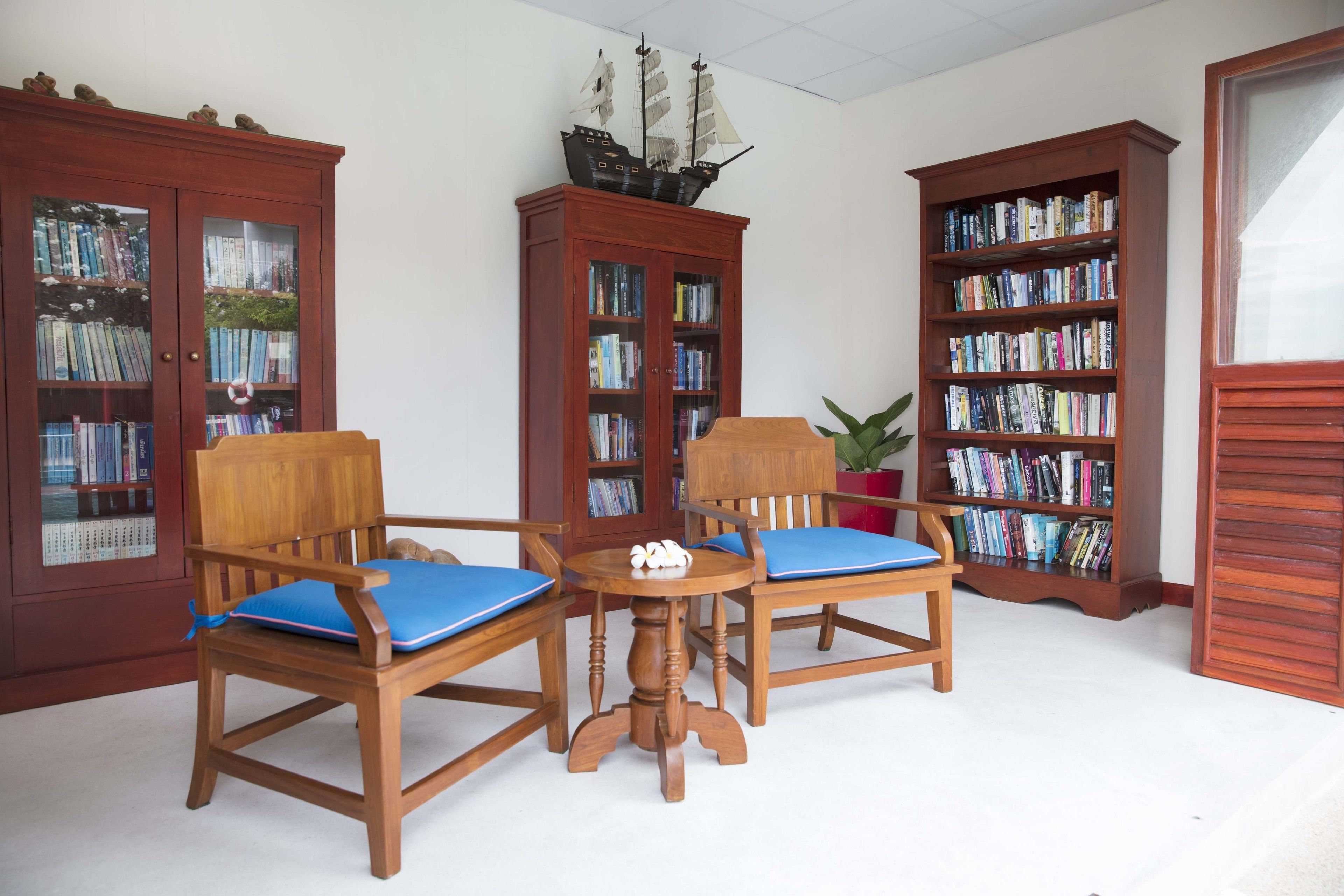 Une pièce comprenant deux chaises en bois avec des coussins bleus, une petite table en bois et une bibliothèque remplie de livres.