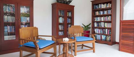 Une pièce comprenant deux chaises en bois avec des coussins bleus, une petite table en bois et une bibliothèque remplie de livres.