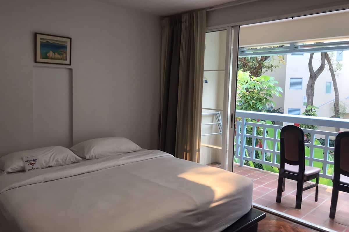 A bedroom with a bed, a painting on the wall, and a balcony with chairs and a railing.